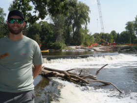 Aaron Schiller, fisheries biologist with Wisconsin Department of Natural Resources, stands by Kletzsch Dam in August 2023 as the fishway is constructed beyond on the east bank.