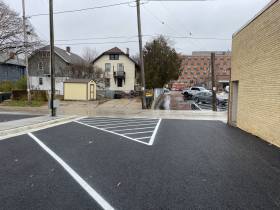A foreground porous parking lot allows rainwater to infiltrate while the rain-slick impervious asphalt lot is seen beyond the alley