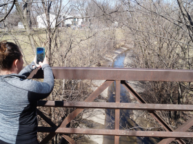Maria Chilbert photographs Wahl Creek from a walking bridge over the waterway as it flows into Lincoln Creek near 47th and Congress on March 9, 2024 during a walk co-led by Nearby Nature and River Revitalization Foundation to celebrate Harriet Tubman Day