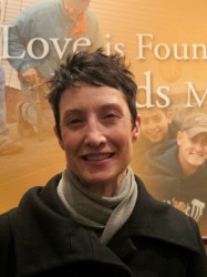 Rose Herriges stands in front of a wall hanging that McComas pointed out during his presentation. It reads, “Love is found in deeds more than words.” (Photo by Jennifer Reinke)