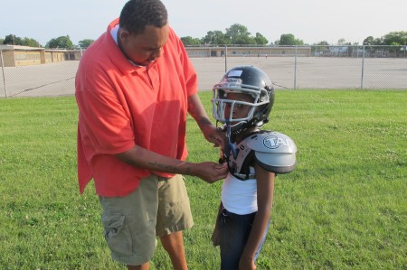 Rodney Hudson helps his son, Rodney, Jr. , with his shoulder pads. (Photo by Edgar Mendez)