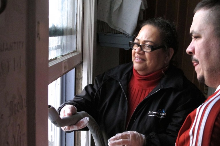 Carmen Reinmund (left) vacuums chipped lead paint from a windowsill as South Side homeowner Armando Martinez watches. Photo by Wyatt Massey.
