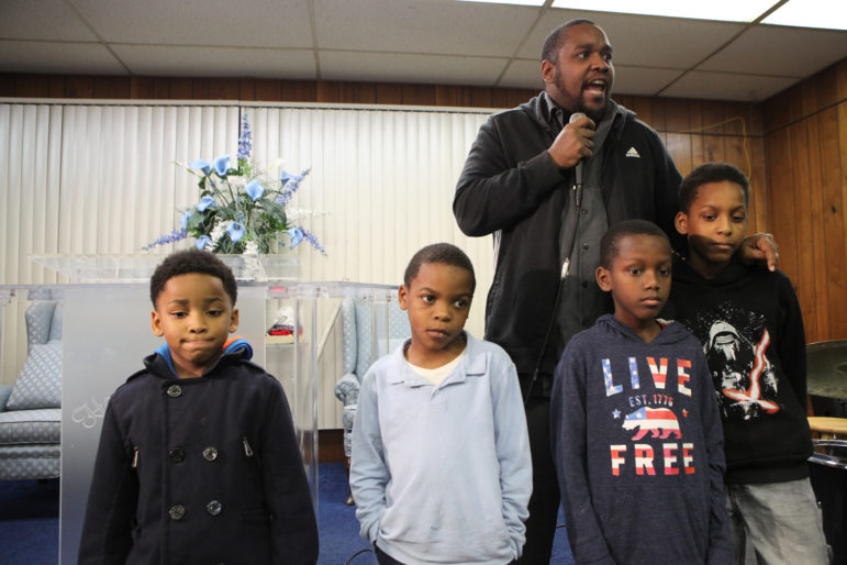 Tory Lowe helped to organize a meeting about lead in drinking water at the House of Prayer in Milwaukee on Dec. 6. He asked the young boys in the audience to join him at the front of the room to challenge everyone to protect them from the dangers of lead in drinking water. The children, from left, are Tomairus Brown, 5, Diamante Silas, 7, Jakoda Eiland, 8, and Jeriko Eiland, 11. Photo by Coburn Dukehart of the Wisconsin Center for Investigative Journalism.