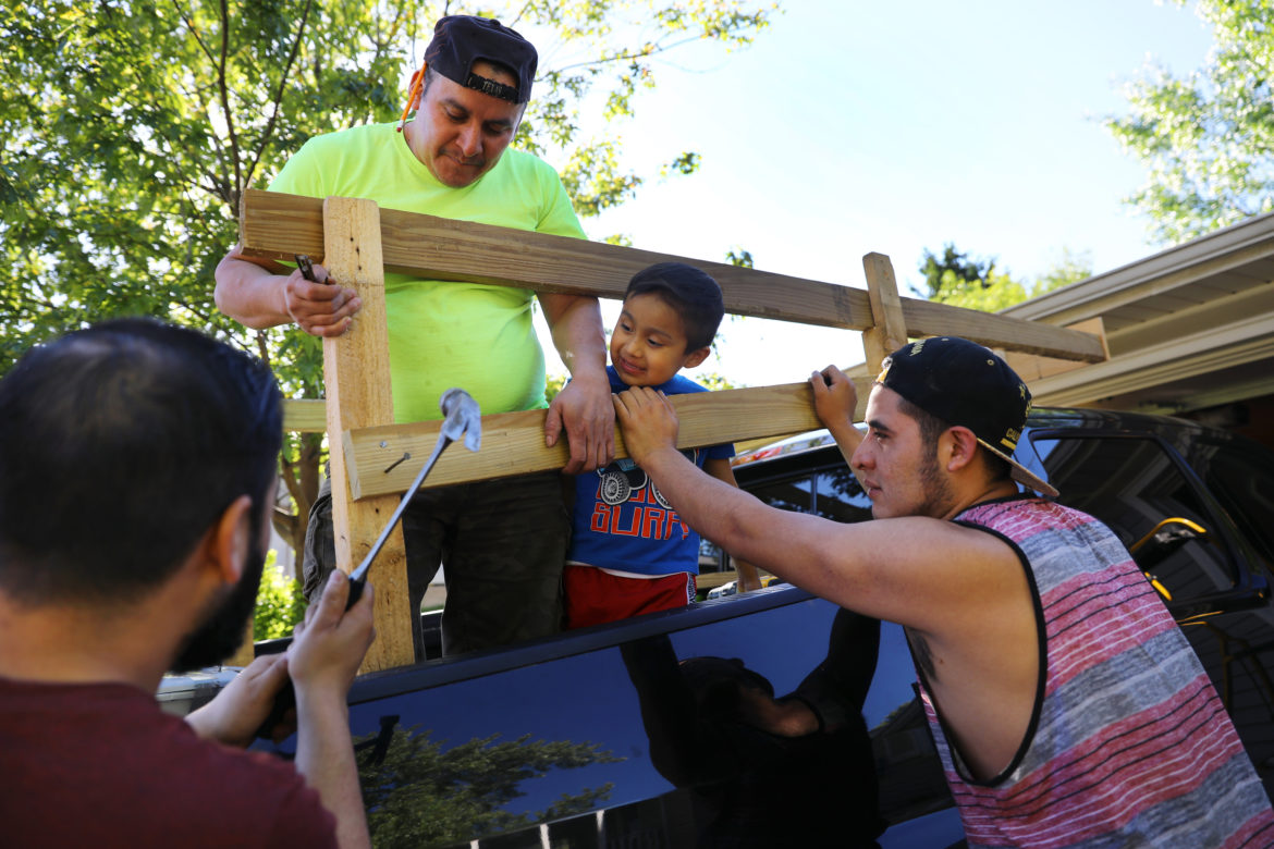 Miguel Hernandez, left, along with co-worker Pedro Tepole, center, and his cousin Eric Hernandez, build a structure on the back of Miguel's pickup truck on May 31, to help carry their belongings to Mexico. Miguel's son, Thomas Hernandez, 5, watches the construction project. Hernandez and Tepole, along with three other dairy workers, left for Mexico the following morning. Photo by Coburn Dukehart of the Wisconsin Center for Investigative Journalism.