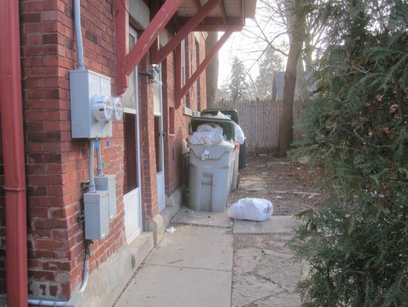 The garbage and recycling bins are overfull, and a bag sits on the ground. Photo by Michael Horne.