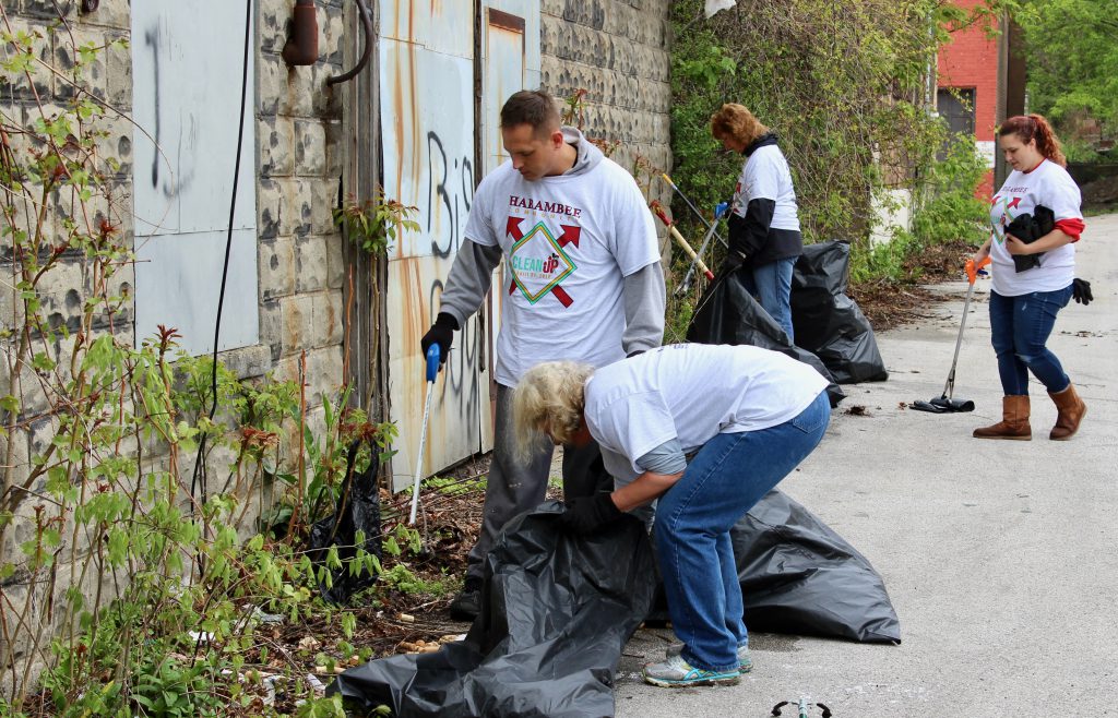 Volunteers scoop debris, including an abandoned collection of wine corks, into trash bags behind a building. Photo by Mark Lisowski.