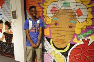 Milwaukee Public Library teen intern Alvin Watts stands in front of his design, which was inspired by his cultural roots in Milwaukee. Photo by Robyn Di Giacinto.