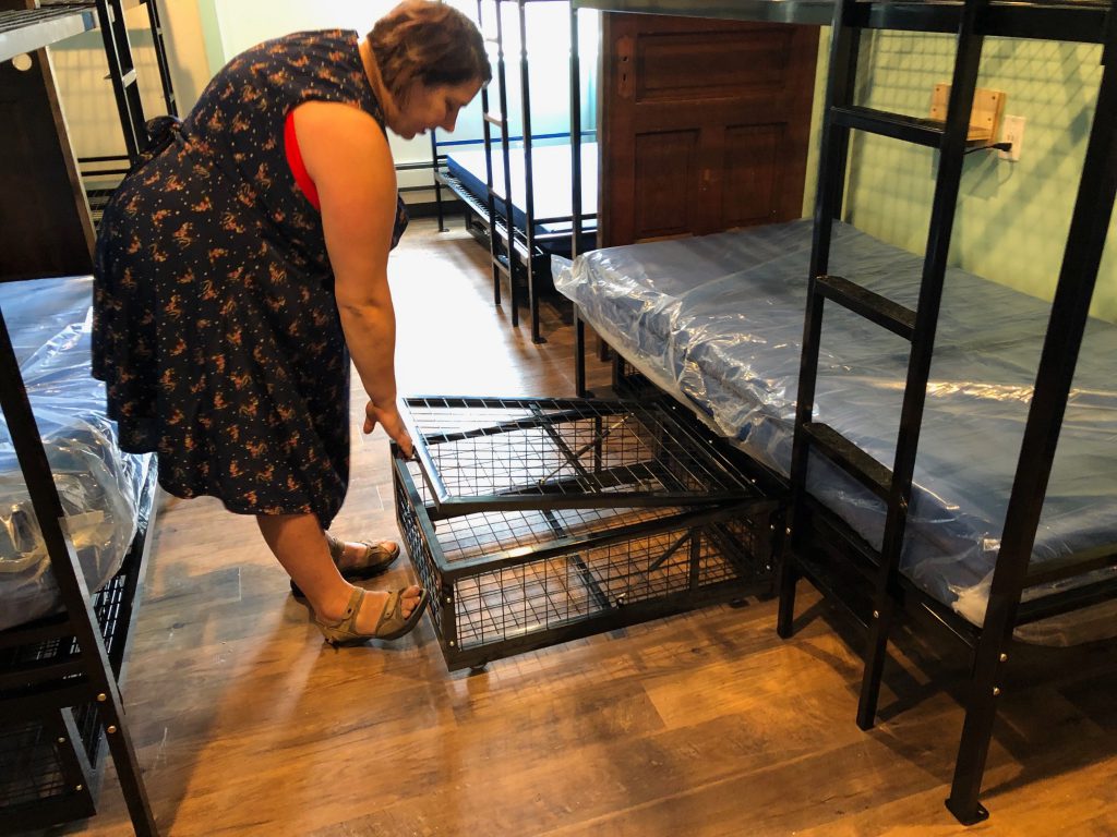 Wendy Mesich demonstrates one of the rolling lockers under bunk beds. The partners are working to complete the rooms in time for a late June opening. Photo by Jeramey Jannene.
