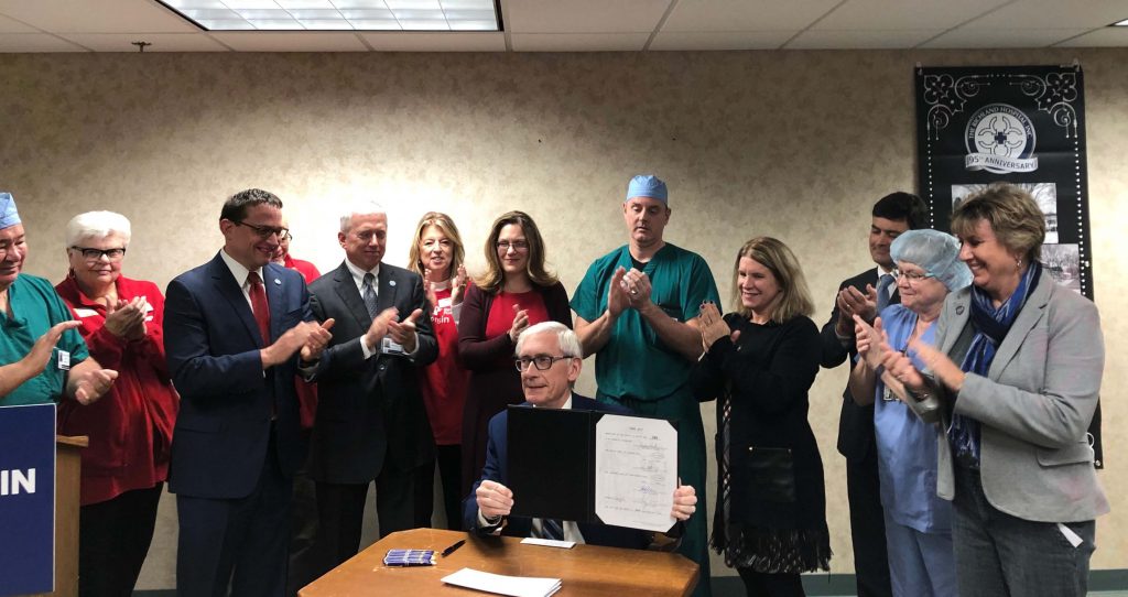 Gov. Tony Evers, seated, after signing Act 56, which expands Medicaid coverage for health care delivered remotely. Photo courtesy of the office of Sen. Jennifer Shilling (D-La Crosse), right. Photo from Shilling's office.