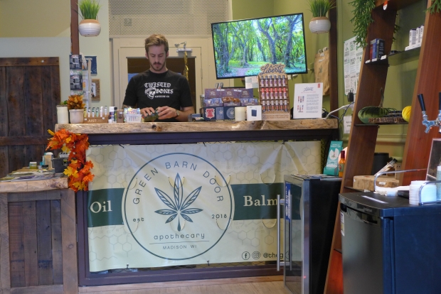 Ryan Barnes works at The Green Barn Door, a retail store which sells CBD products on State Street in Madison. In this Dec. 2019 photo, Barnes measures CBD hemp buds. Photo by Shamane Mills/WPR.