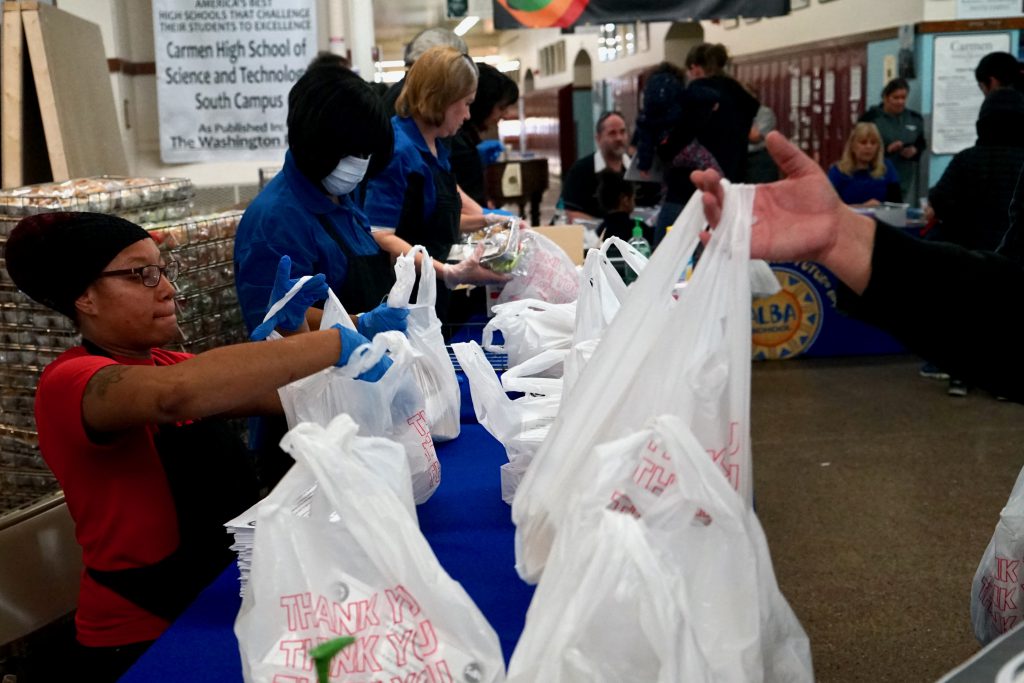 An assembled team of MPS staff distributes sack lunches and packets of educational materials Monday at ALBA Elementary. (Photo by Adam Carr)