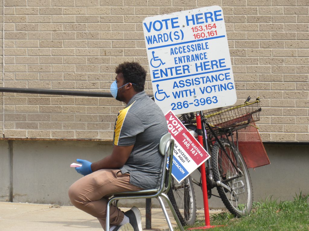 A poll worker sits outside of Washington High School wearing a protective mask. Photo by Isiah Holmes/Wisconsin Examiner.