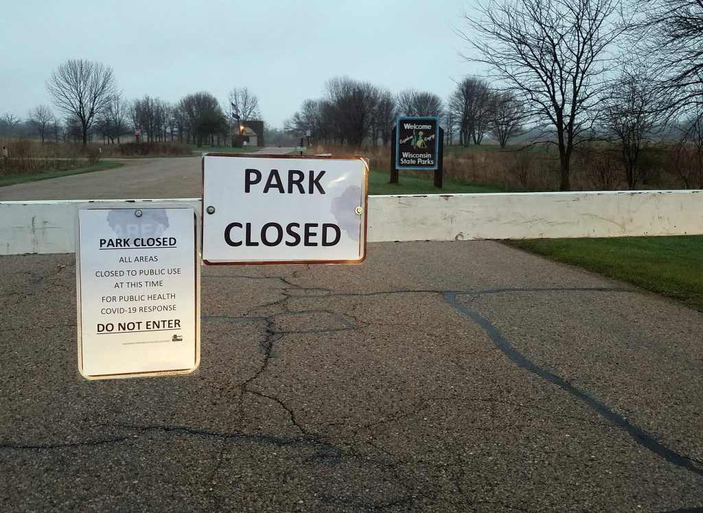 Governor Nelson State Park in Dane County was one of dozens of state parks in Wisconsin ordered closed on April 9, 2020 due to overcrowding and other issues amid the COVID-19 pandemic. Most state parks were ordered to reopen on May 1 with reduced capacity limits, distancing requirements and other changes in place. This photo from April 29 shows a sign at a park entrance noting the closure. Photo by Kristian Knutsen/WisContext.