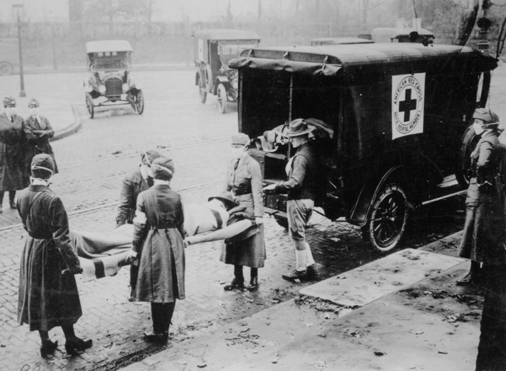 Masked American Red Cross attendants in St. Louis remove the body of a flu victim in 1918, a common scene in cities around the country at the time of the pandemic. Wisconsin was the only state to confront the 1918 flu pandemic with uniform, statewide shutdown measures, which limited deaths, historians say. Photo courtesy of the National Archives/Wisconsin Watch.