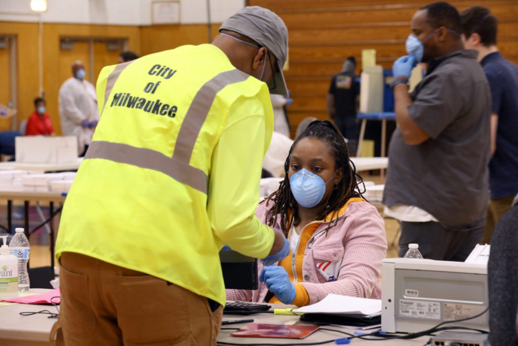 A poll worker assists a city of Milwaukee employee with check-in at Marshall High School in Milwaukee on April 7, 2020. Wisconsin voters in central and northern Wisconsin head to the polls again during the pandemic to fill the 7th Congressional District seat. Photo by Coburn Dukehart/Wisconsin Watch.