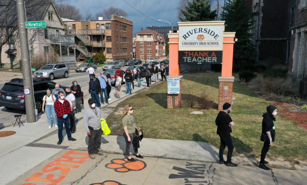 The voting line wraps around the block outside Riverside High School in Milwaukee during the primary election on April 7, 2020. A new report says the city’s voter turnout was strongly depressed by Milwaukee’s decision to reduce its normal 182 polling sites to five and voter fears of contracting COVID-19. Photo by Coburn Dukehart/Wisconsin Watch.
