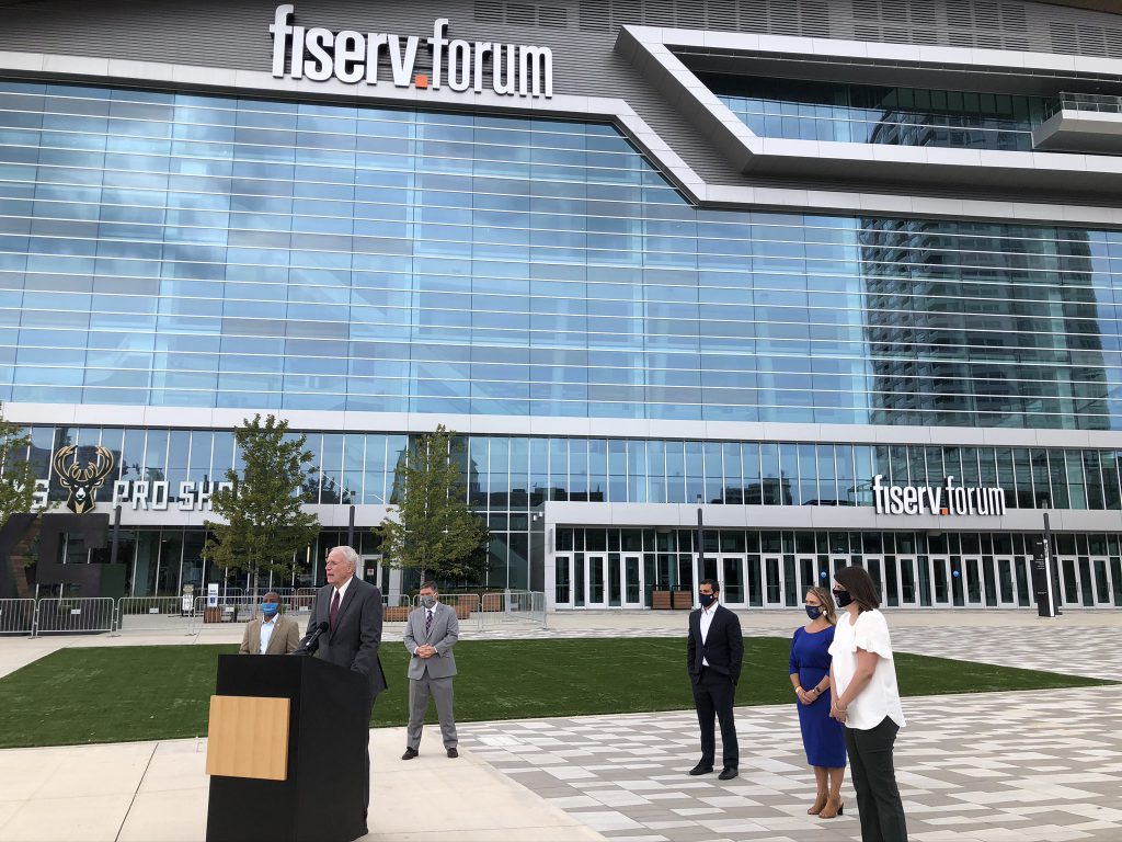 Mayor Tom Barrett speaks outside Fiserv Forum as council president Cavalier Johnson, county clerk George Christenson, Bucks vice president Alex Lasry, Brewers director Leslie Stachowiak and Milwaukee election commission director Claire Woodall-Vogg look on. Photo by Jeramey Jannene.
