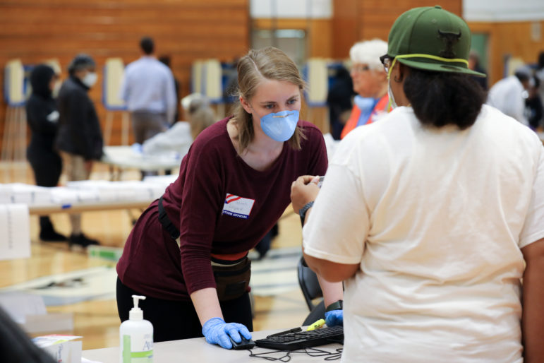 A poll worker wearing protective gear assists a voter at Marshall High School in Milwaukee on April 7, 2020. Wisconsin faces multiple lawsuits from plaintiffs with disabilities seeking additional accommodation to make voting more accessible in the November election. Photo by Coburn Dukehart / Wisconsin Watch.