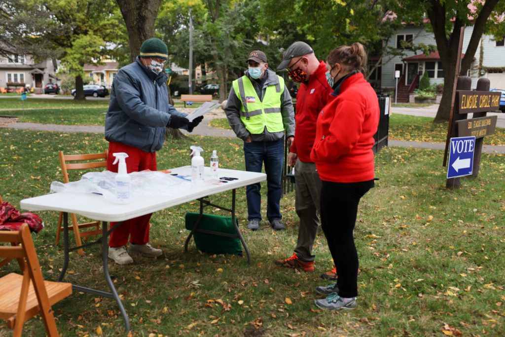 Volunteer poll worker Steve Klafka accepts absentee ballots from Sam and Sunny McDaniel in Elmside Circle Park in Madison, Wis., on Oct. 3, 2020. Also pictured is volunteer poll worker Jeremy Stoddard. The Madison City Clerk's Office held Democracy in the Park events to register voters, answer questions about the voting process and accept the delivery of absentee ballots on Sept. 26 and Oct. 3, 2020. Some social media users sought to falsely portray the event as illegal. Coburn Dukehart/Wisconsin Watch