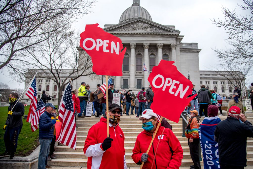 Protesters are seen at a rally at the Wisconsin State Capitol on April 24, 2020. They were demanding an end to the wide-ranging shutdown of normal life and business in Wisconsin aimed at curbing the coronavirus pandemic. Weeks later, Gov. Tony Evers’ Safer at Home order was overturned by the Wisconsin Supreme Court. Even as the state’s pandemic death toll surges, some Wisconsin residents believe the threat of COVID-19 is overblown, that masks are dangerous and restrictions to curb the disease are part of a plot to ruin the economy and make people dependent on the government. Will Cioci / Wisconsin Watch