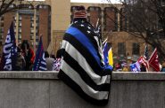 A rally attendee sits draped in a "Thin Blue Line" pro-police blanket. Photo by Henry Redman/Wisconsin Examiner.