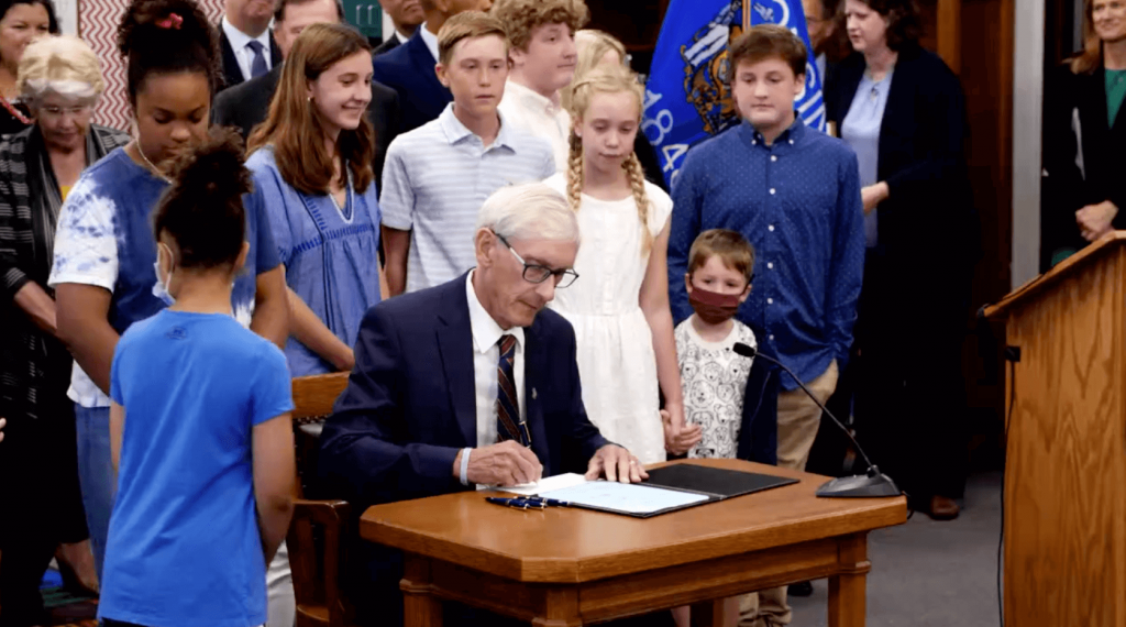 Gov. Tony Evers signs the 2021-23 biennial budget at Cumberland Elementary School in Whitefish Bay, after making 50 partial vetoes. Screenshot from Gov. Evers Facebook video/Wisconsin Examiner.