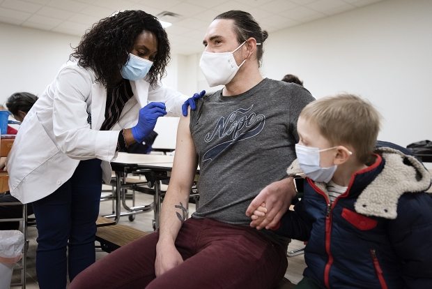 Scott Mizzen of Milwaukee holds hands with his son, Harrison, as he receives a COVID-19 vaccine Thursday, March 11, 2021, at Hayat Pharmacy in Milwaukee, Wis. Angela Major/WPR