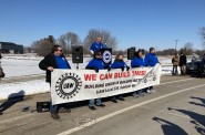 UAW Local 578 President Bob Lynk addresses a rally at Oshkosh Corp. calling on the company to build new postal trucks in Wisconsin instead of a nonunion plant in South Carolina. Members of the local’s bargaining committee stand in front. Photo by Miles Maguire/Wisconsin Examiner.