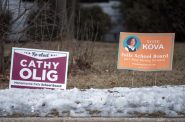 Signs for Cathy Olig, a board member up for reelection this year in Menomonee Falls, and Kova Brown, another school board candidate, are displayed at a home near Menomonee Falls High School on Saturday, Feb. 12, 2022, in Menomonee Falls, Wis. Angela Major/WPR