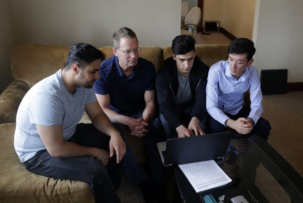 Mike Ruminski, second from left, helps Muddassir Saboory, Fayaz Nabizada and Ali Akbar Gholami work on the computer in their duplex on April 10, 2022, in Allouez, Wis. (Sarah Kloepping/USA TODAY NETWORK-Wisconsin)