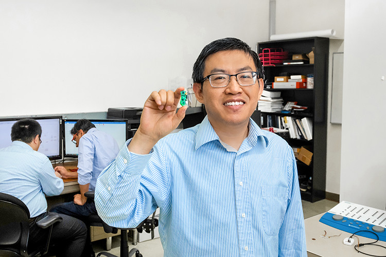 Yi Hu, an associate professor of electrical engineering at UW-Milwaukee, holds an early version of his over-the-counter hearing aid prototype in his campus lab. Hu and his team have revised the design, which is about half the size of the earlier model. Photo courtesy of Elora Lee Hen, UW-Milwaukee