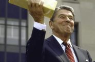 President Ronald Reagan holds up a block of government surplus cheese during an event in 1985. When it began in 1939, federal food assistance consisted primarily of surplus goods purchased from farmers and food producers. Over the decades, it evolved into the food stamp program. Now, recipients use electronic benefit transfer cards to purchase groceries. But some long-lasting barriers remain, including a cumbersome process to maintain benefits. (Dirck Halstead / Getty Images)