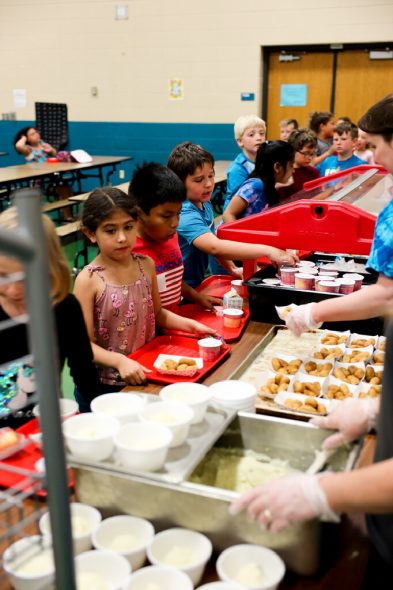 Second and third graders at Janet Berry Elementary School in Appleton, Wis., stand in the lunch line to receive free school meals on June 2, 2022. From left are Aria Montes, Lucas Chavez, Tyler Parke, Elina Singh, Brady Dyreson, Azariah Hammerstad and Ethan Lemke. Chavez, in the red shirt, says he ate school lunch more during the free meal program than before the pandemic, which was easier for him because he said he sometimes forgot his lunch money. (Amena Saleh / Wisconsin Watch)