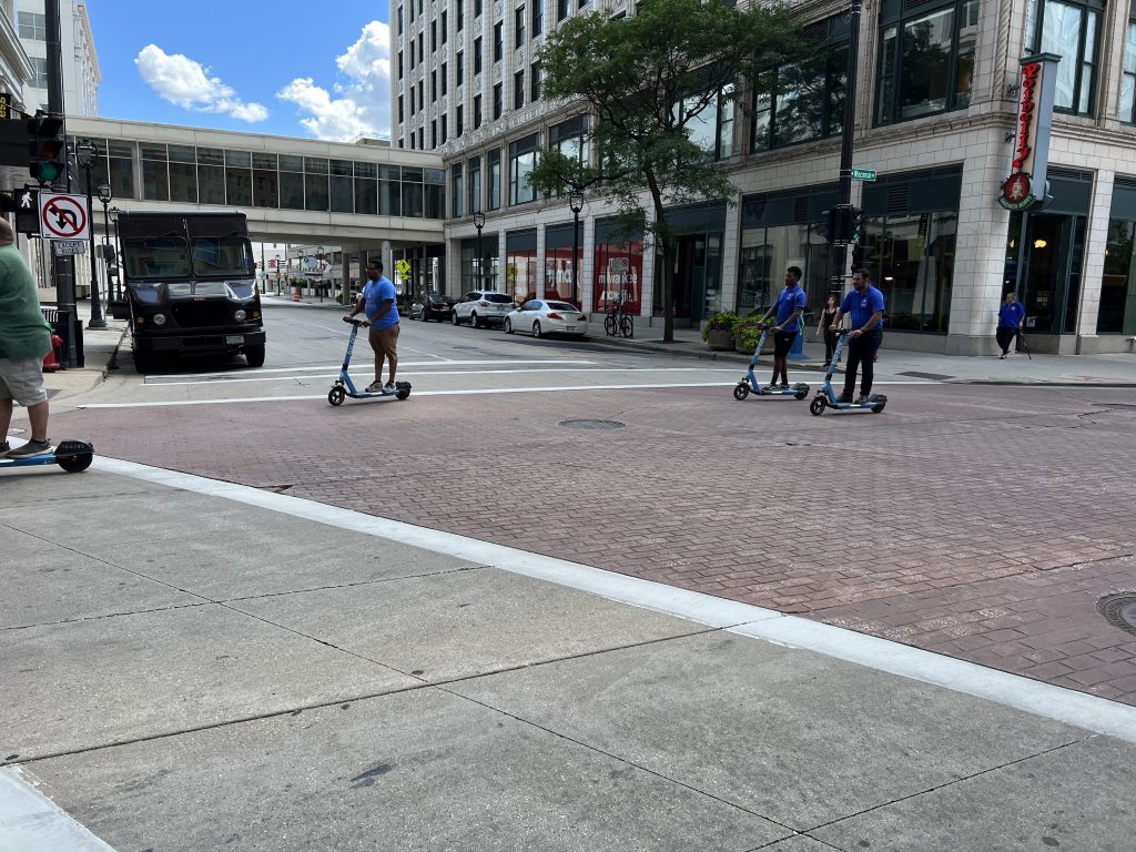 Individuals ride Blue Duck scooters in downtown Milwaukee outside the company's new office. Photo by Jeramey Jannene.