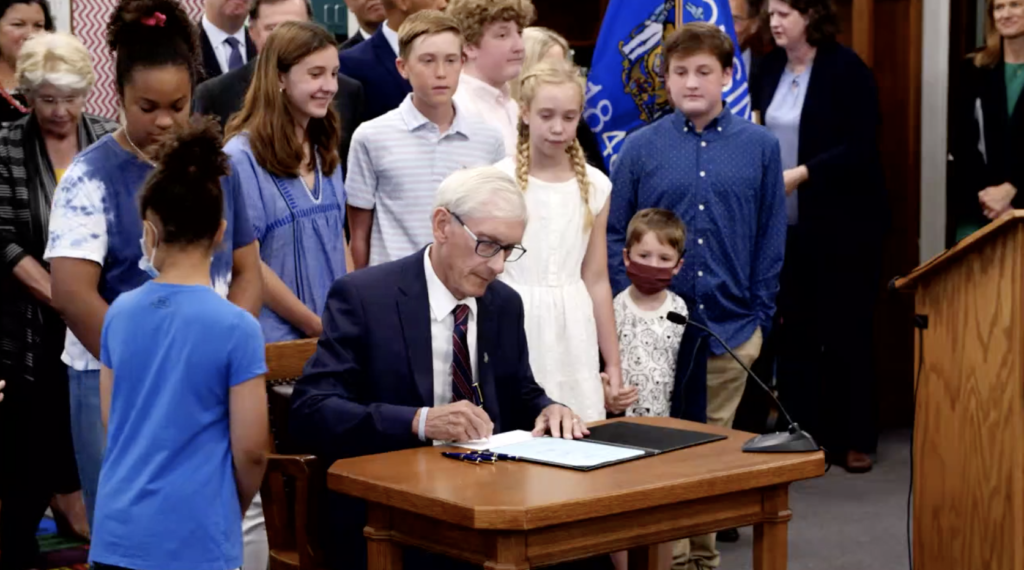 Gov. Tony Evers signs the 2021-23 budget at Cumberland Elementary School in Whitefish Bay on July 8, 2021, after making 50 partial vetoes. An Evers administration report Monday forecasts a $6.5 billion state surplus by the end of the current budget. (Screenshot | Gov. Evers Facebook video)