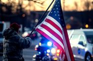 An onlooker holds a flag as the hearse passes during a procession Monday, Feb. 13, 2023, in honor of Milwaukee police officer Peter Jerving in Brookfield, Wis. Jerving was shot and killed in the line of duty. Angela Major/WPR
