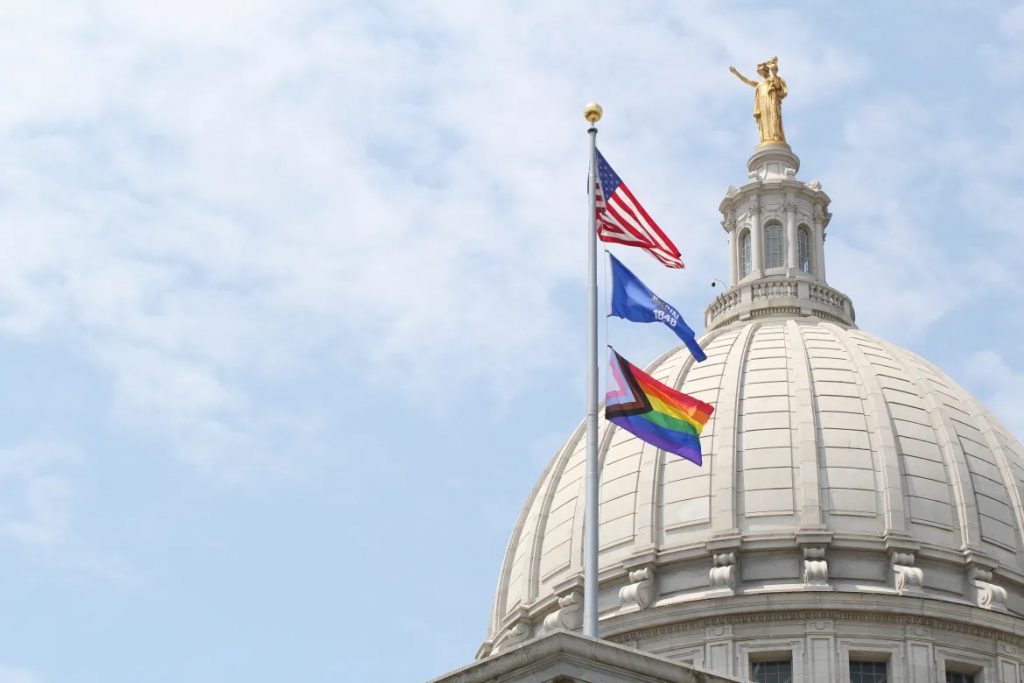 A Progress Pride flag flies above the Wisconsin State Capitol’s east wing. Wisconsin is one of two states that refer to a “husband” in the statutory definition of parent. Attempts to change that have stalled in the Republican-controlled Legislature. (Drake White-Bergey / Wisconsin Watch)