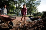 Jalyssa Ferguson, 8, holds a wheelbarrow for Janiah Torres, 10, who fills it with mulch as residents of Milwaukee’s Valley Park neighborhood participate in a park cleanup on July 13, 2023. Residents worry that a $1.2 billion plan to widen the Interstate 94 East-West Freeway corridor will lead to more flooding in the area, undoing their work on the park. (Pat A. Robinson for Wisconsin Watch)