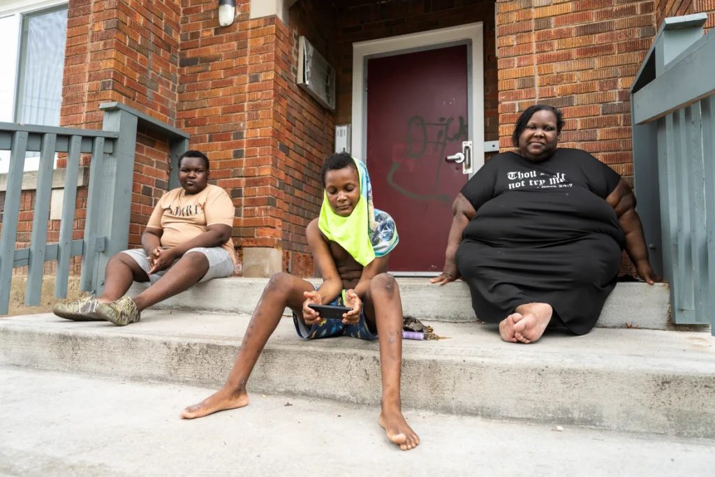 Jaidyn Jordan, 12, and Aidan Branch, now 10, sit with their mother Deanna Branch on the front stairs of a Milwaukee apartment they were moving out of on July 1, 2023. Beginning in 2015 Aidan was twice sent to Children’s Wisconsin hospital with severe lead poisoning due to hazards in a previous rental. Branch broke that lease and moved the family while waiting on the landlord to address the home’s lead hazards. She faced a lawsuit as a result. (Sara Stathas for Wisconsin Watch)