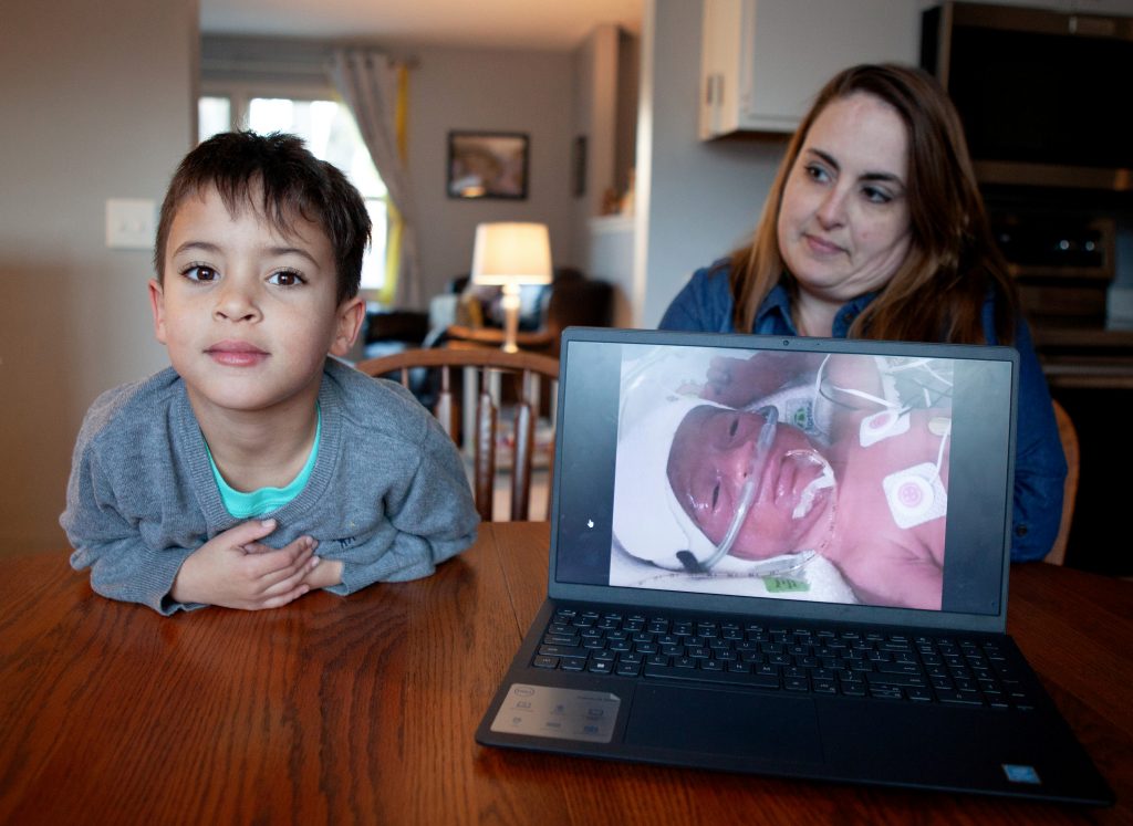 Emily Schmit, 37, and her son, Armoni Meyers, 6, of Mount Horeb, Wis., with a photo of Armoni in the NICU after being born three months premature in 2018. Schmit is an advocate for mothers in the state's BadgerCare Plus Medicaid program to receive medical care for a full year after giving birth, something she didn't have after Armoni was born. (Brad Horn for Wisconsin Watch)