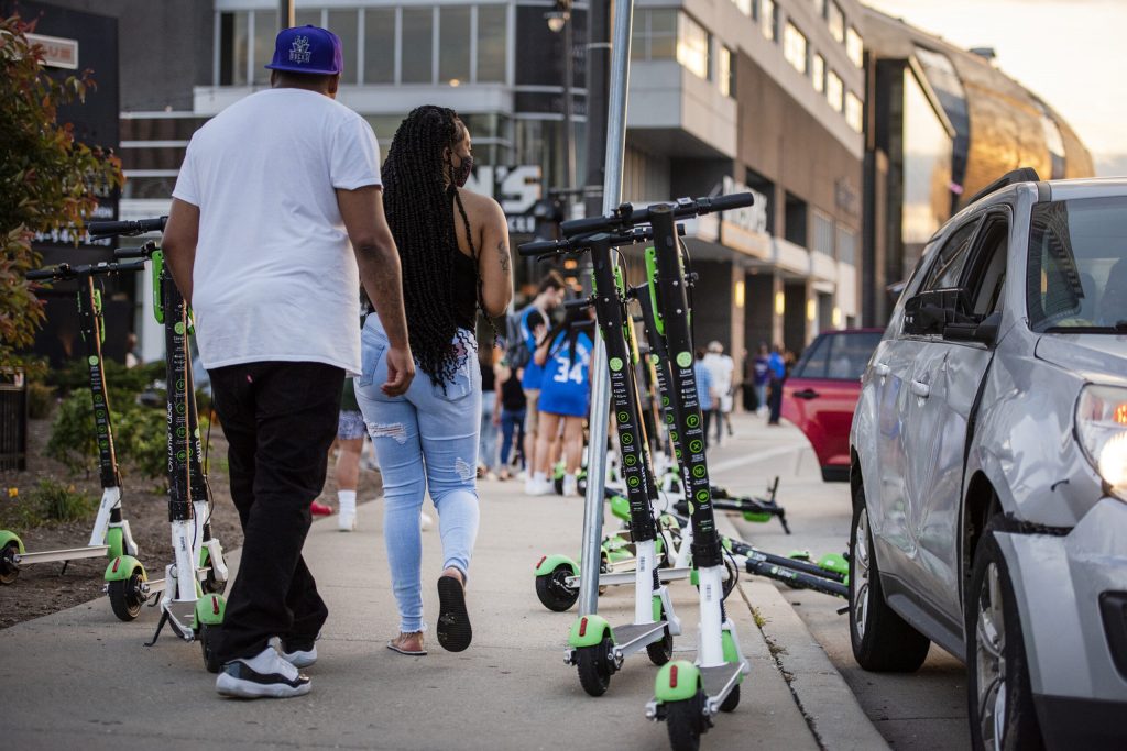 People walk past electric scooters parked on a sidewalk Wednesday, June 23, 2021, in downtown Milwaukee, Wis. Angela Major/WPR