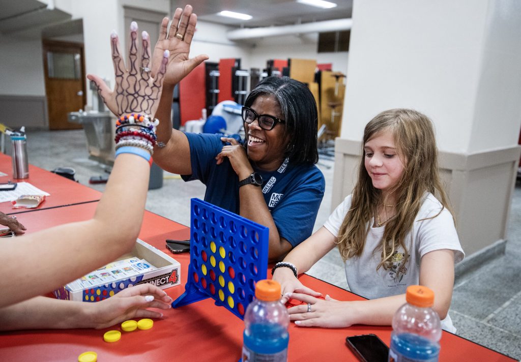 Youth leader Angela Allgood, center, gives a high five while playing Connect 4 with students Wednesday, July 12, 2023, at Bay View High School in Milwaukee, Wis. Angela Major/WPR