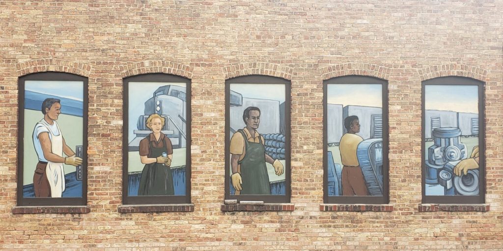 A new report finds that even with Wisconsin's record employment growth, the boom hasn't benefited all parts of the state. A mural depicting workers is painted on windows of the Madison-Kipp Corp. The artwork was created by Goodman Community Center students and Madison-Kipp employees with Dane Arts Mural Arts. (Erik Gunn | Wisconsin Examiner)