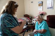 Arlene Meyer, 86, of Gleason, right, smiles as Paula Streich, a certified nursing assistant, left, opens a chocolate bar she brought for Meyer on Nov. 15, 2024, at Pine Crest Nursing Home in Merrill, Wis. Meyer said Streich often brings her gifts from outside the nursing home like chocolate bars. (Joe Timmerman / Wisconsin Watch)