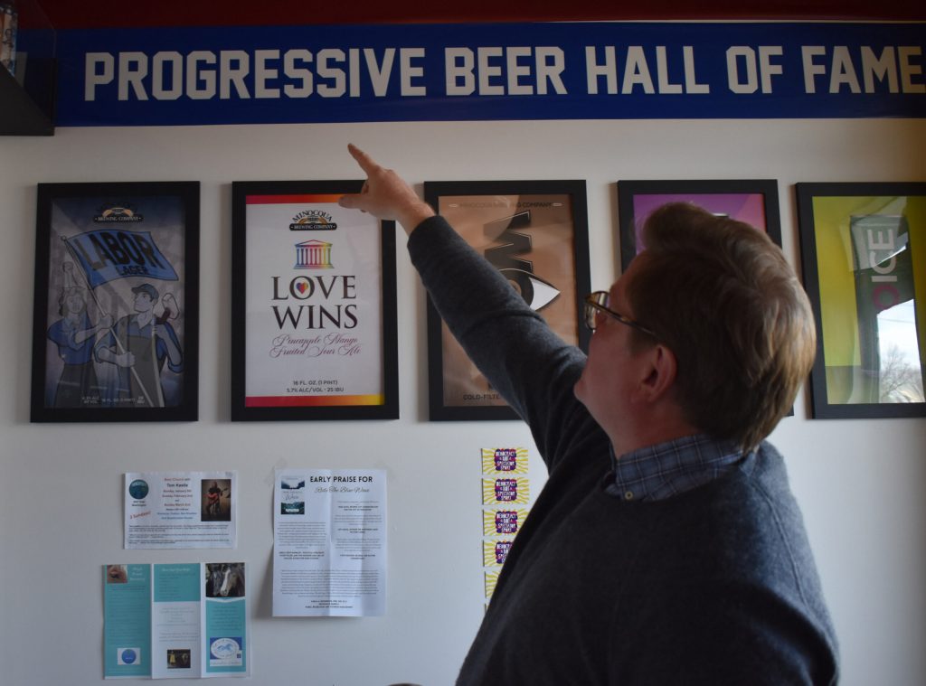 Kirk Bangstad points out the “Progressive Beer Hall of Fame” at the Minocqua Brewing Company Madison Taproom. Rob Mentzer/WPR