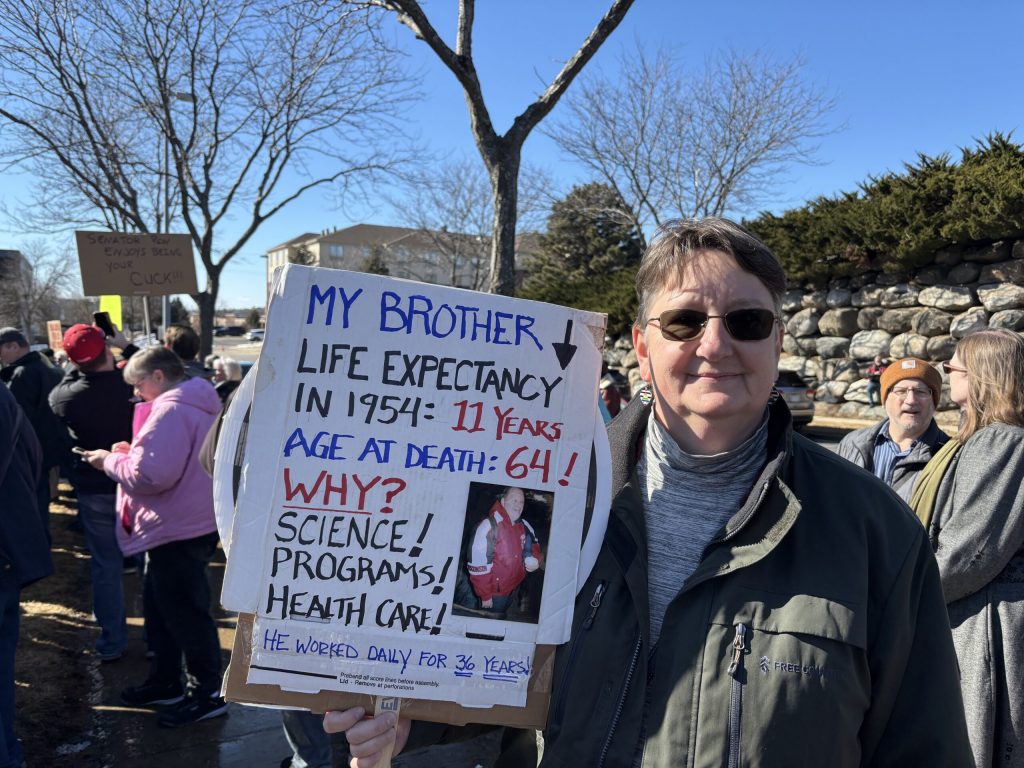 Appleton resident Dorothy Witzeling attends a Madison protest against potential Medicaid cuts. She holds a sign with a photo of her brother who relied on the government program. Addie Costello/WPR