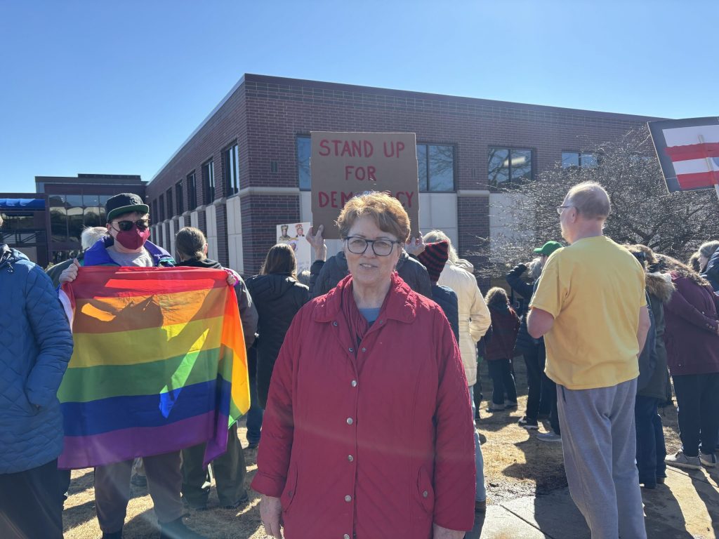 Protest organizer Laurine Lusk stands in front of a large crowd chanting and singing together in front of U.S. Sen. Ron Johnson’s Madison office. Addie Costello/WPR