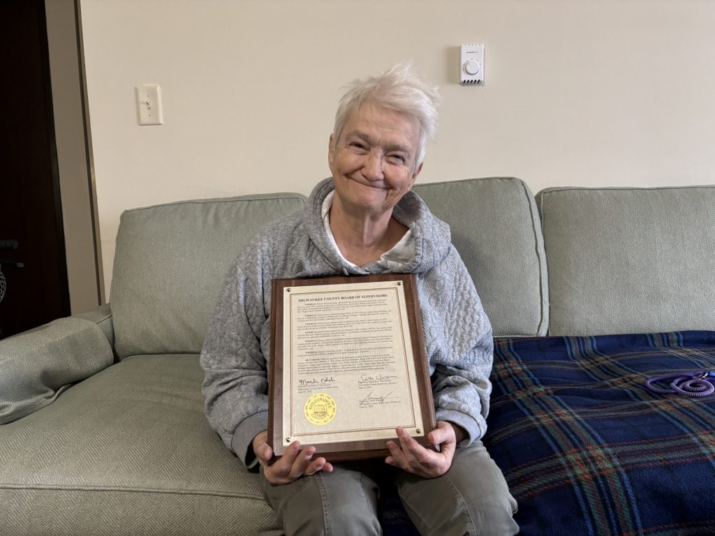 Sharon Dixon poses with a plaque from the Milwaukee County Board of Supervisors recognizing her contributions to the LGBTQ+ community, at her apartment in Franklin. Beatrice Lawrence/WPR