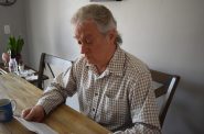 Neenah resident Tom Frantz reads a print-out of the email he received from federal immigration officials, which told him to leave the country, at his kitchen table on Thursday, April 17, 2025. Joe Schulz/WPR