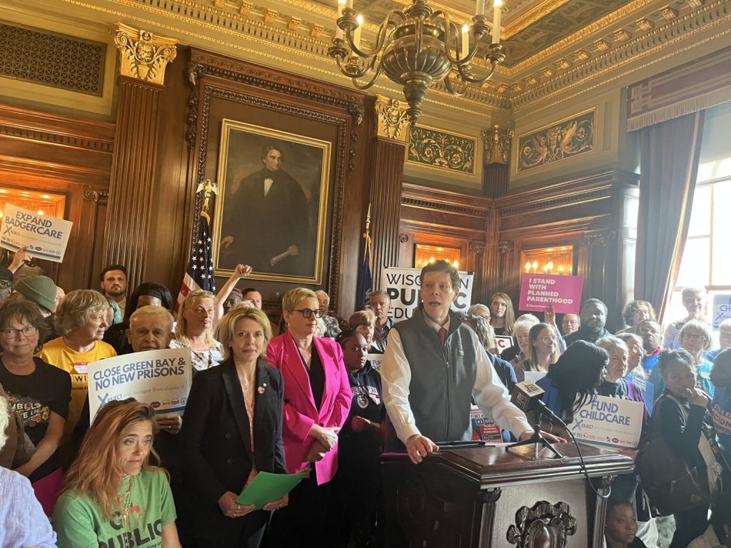 Robert Kraig of Citizen Action at the podium in the Senate parlor in the Wisconsin State Capitol on Tuesday, May 27 , surrounded by representatives of other grassroots groups | Ruth Conniff/Wisconsin Examiner